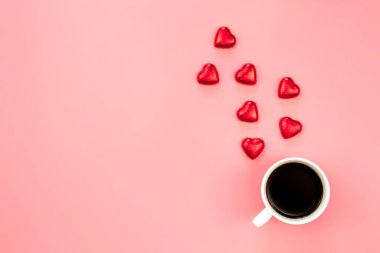 Cup of coffee and heart shaped sweets on a pink background, flat lay, copy space.