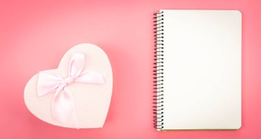 Blank notebook and heart shaped gift box on pink background, top view, copy space.