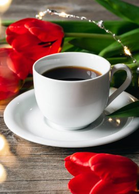 Spring composition with a cup of coffee and red tulips on a wooden surface, close up.
