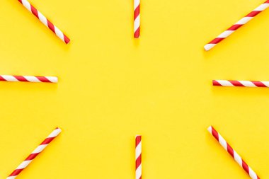 Party drinking straws arranged into a circle on yellow background, flat lay, copy space.