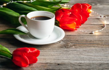 Spring composition with a cup of coffee and red tulips on a wooden surface, copy space.