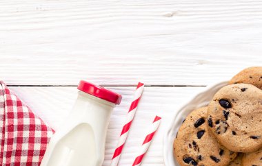 Bottle of milk, paper straws and cookies with chocolate, flat lay, copy space.