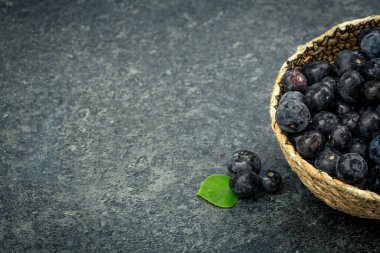 Blueberries in a bowl on a textured black background, copy space.