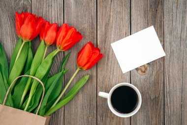 Bouquet of red tulips, a cup of coffee and a blank sheet for wishes, space for text, top view.