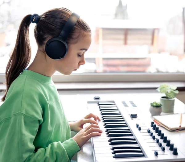 Little girl in headphones learning to play the piano at home, music lesson, learning.