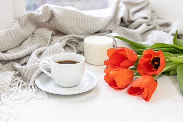 Cozy spring composition with a cup of coffee, red tulips and a candle.