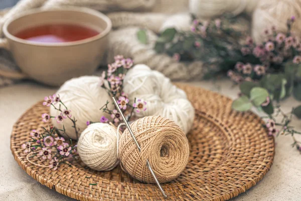 Cozy composition with knitting threads, a cup of tea and flowers on a blurred background.