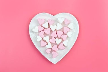 Heart shaped plate with heart shaped marshmallows on pink background, flat lay.