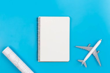 An airplane miniature, map and notebook on blue background, flat lay, tourism and travel concept, copy space.