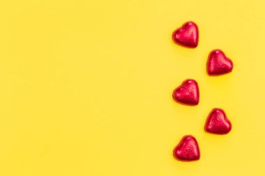 Red heart shaped chocolate candies on yellow background isolated, flat lay, copy space.