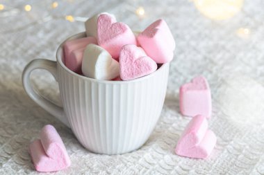 A cup with pink and white heart-shaped marshmallows, close-up, blurred background with bokeh.