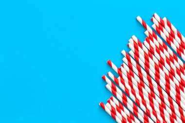 Drinking straws for party on blue background, copy space. Top view of red paper disposable, eco-friendly straws for summer cocktails.