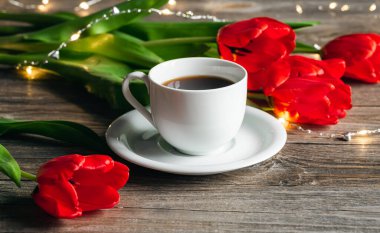 Spring composition with a cup of coffee and red tulips on a wooden surface, close up.