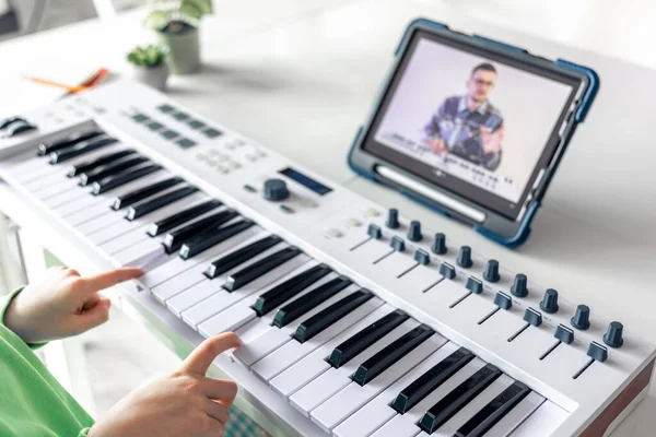 Little girl learns to play the piano with teacher online, distance learning music, music lesson at home with a tablet.