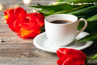 Spring composition with a cup of coffee and red tulips on a wooden surface.