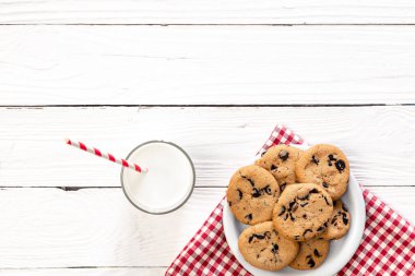 Plate with chocolate chip cookies, and a glass of milk on a wooden background, flat lay.