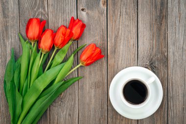 Bouquet of red tulips and a cup of coffee on a wooden background, top view, copy space.
