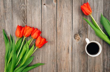 Bouquet of red tulips and a cup of coffee on a wooden background, top view, copy space.