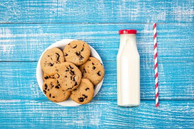 A bottle of milk, a plate of cookies and a paper straw, flat lay, rustic style.