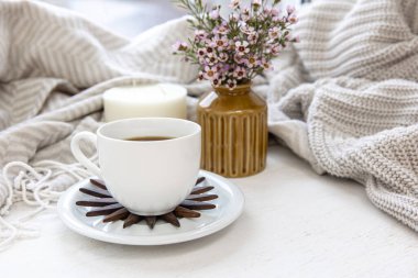 Home composition with a cup of coffee, a plaid, a candle and a bouquet of wild flowers.