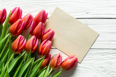 A bouquet of pink tulips and a piece of paper for text on a wooden background, top view, copy space.