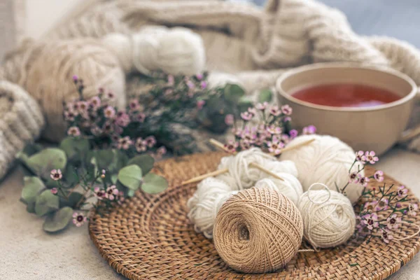 Cozy composition with knitting threads, a cup of tea and flowers on a blurred background.