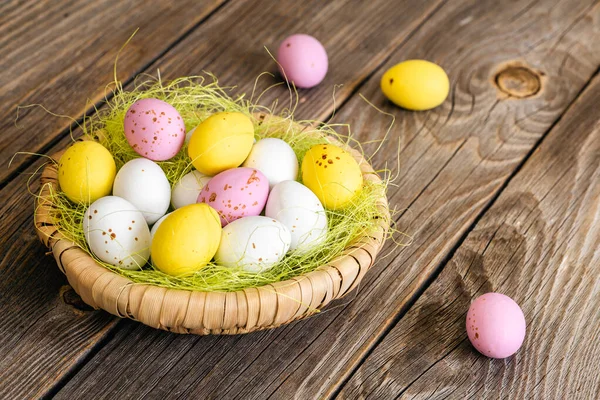 Multi-colored eggs, Easter dessert for children, egg-shaped candies in a decorative nest on a wooden background.