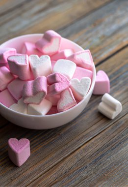 Bowl with pink and white marshmallows in the form of hearts, close-up on a wooden background.