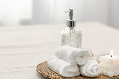 Spa composition with towels, candle and soap dispenser on blurred white background, copy space.