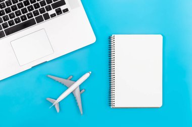 Laptop, airplane miniature and notebook on blue background, flat lay, tourism and travel concept, copy space.
