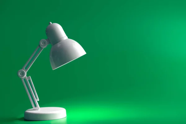 White table lamp on a green background. A small toy lamp, concept of learning, reading and education, copy space.
