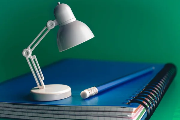 White table lamp on a green background. A small toy lamp on the notebook. The concept of learning, reading and education.