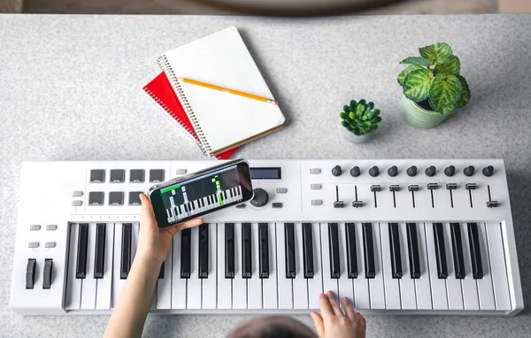 A child learns to play the piano with a smartphone, online music lesson, self-study with the help of video, top view.