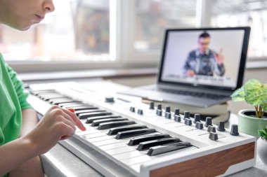 Küçük bir kız öğretmeniyle online piyano çalmayı öğreniyor, uzaktan müzik öğreniyor, evde dizüstü bilgisayarla müzik dersi alıyor..