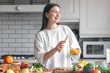 Attractive young woman cutting vegetables for salad in the kitchen, food preparation concept.