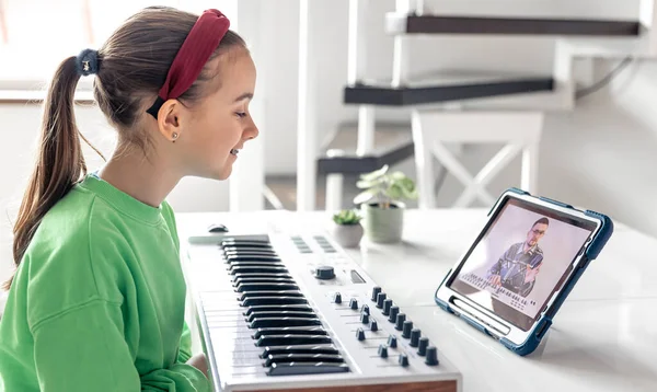 Little girl learns to play the piano with teacher online, distance learning music, music lesson at home with a tablet.