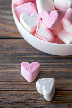 Bowl with pink and white marshmallows in the form of hearts, close-up on a wooden background.