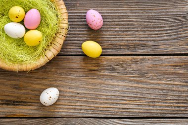 Easter eggs in a decorative nest on a wooden background, top view, copy space, rustic style.