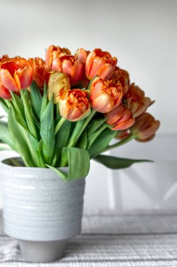 Bouquet of orange tulips in a vase on a table in a room interior.