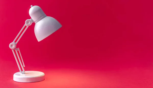 White table lamp on a Viva Magenta background. A small toy lamp, concept of learning, reading and education, copy space.