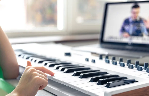 A little girl learns to play piano with teacher online, remote music learning, music lesson at home with laptop.