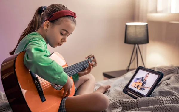 Little girl learns to play the guitar, music lesson with online teacher, distance learning to play the guitar.