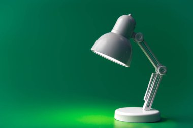 White table lamp on a green background. A small toy lamp, concept of learning, reading and education, copy space.