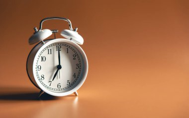 Kahverengi arkaplan üzerindeki beyaz alarm saati izole edildi, kopyalama alanı.