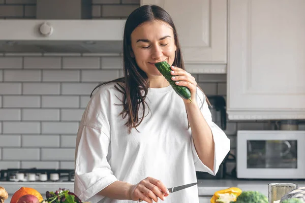 stock image Attractive young woman cutting vegetables for salad in the kitchen, food preparation concept.