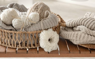 Odanın içindeki ahşap bir bankta örgü örmek için iplik dolu sepet. Örgü konsepti..