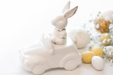 Paskalya arkaplanı, arabada seramik bir tavşan ve beyaz arka planda Paskalya yumurtaları.,