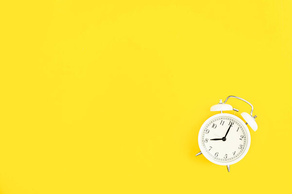 White alarm clock on a yellow background, flat lay, copy space.