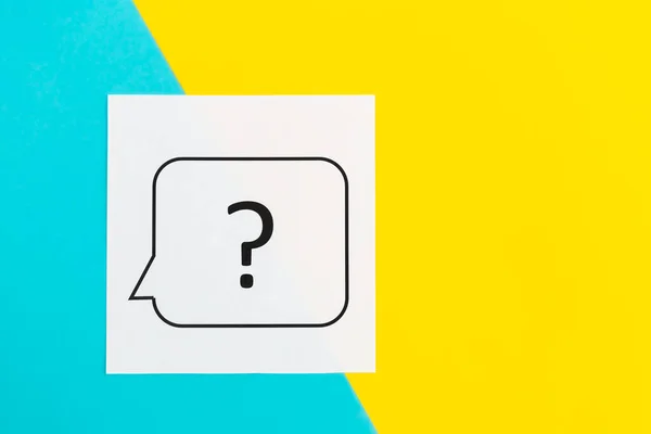 Question mark on white paper on yellow and blue background, flat lay.