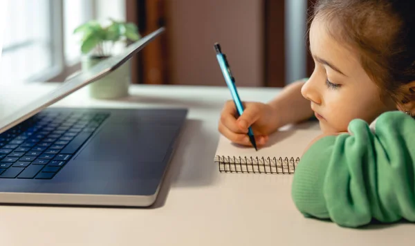 Mała Dziewczynka Pisze Notatniku Siedząc Przed Laptopem Koncepcja Nauki Online — Zdjęcie stockowe
